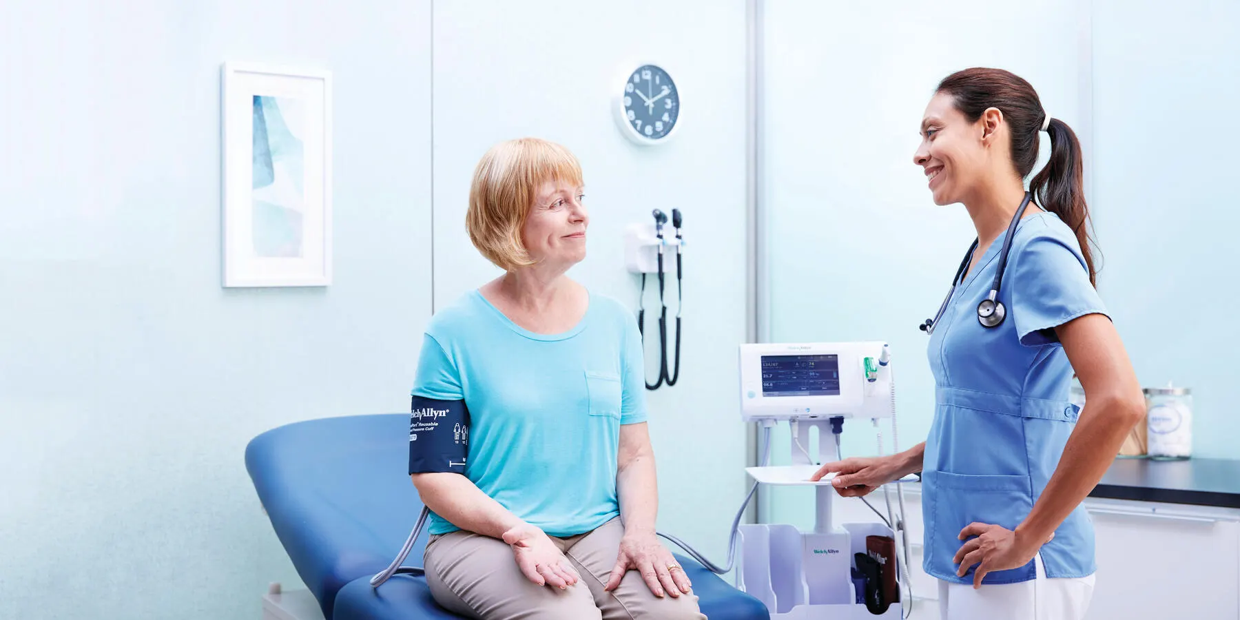 A patient sits in a physician's office while a clinician measures their blood pressure.