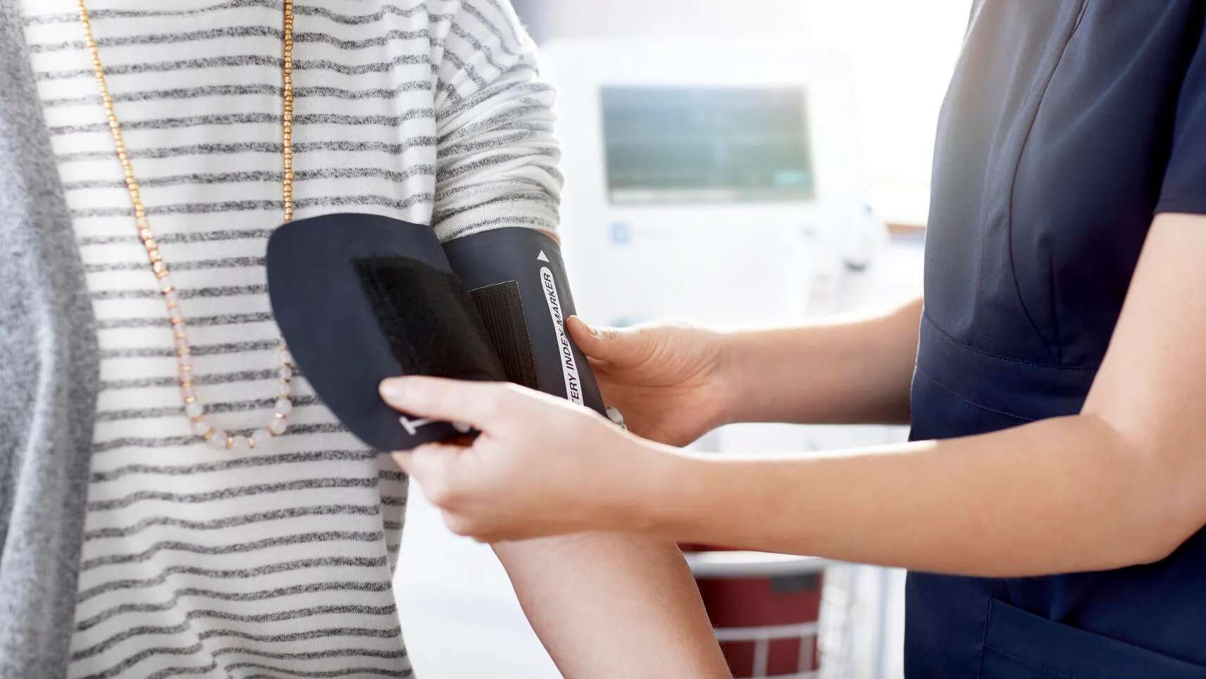 A clinician places a blood pressure cuff on a patient’s arm with a Welch Allyn Spot Vital Signs 4400 Device in the background.