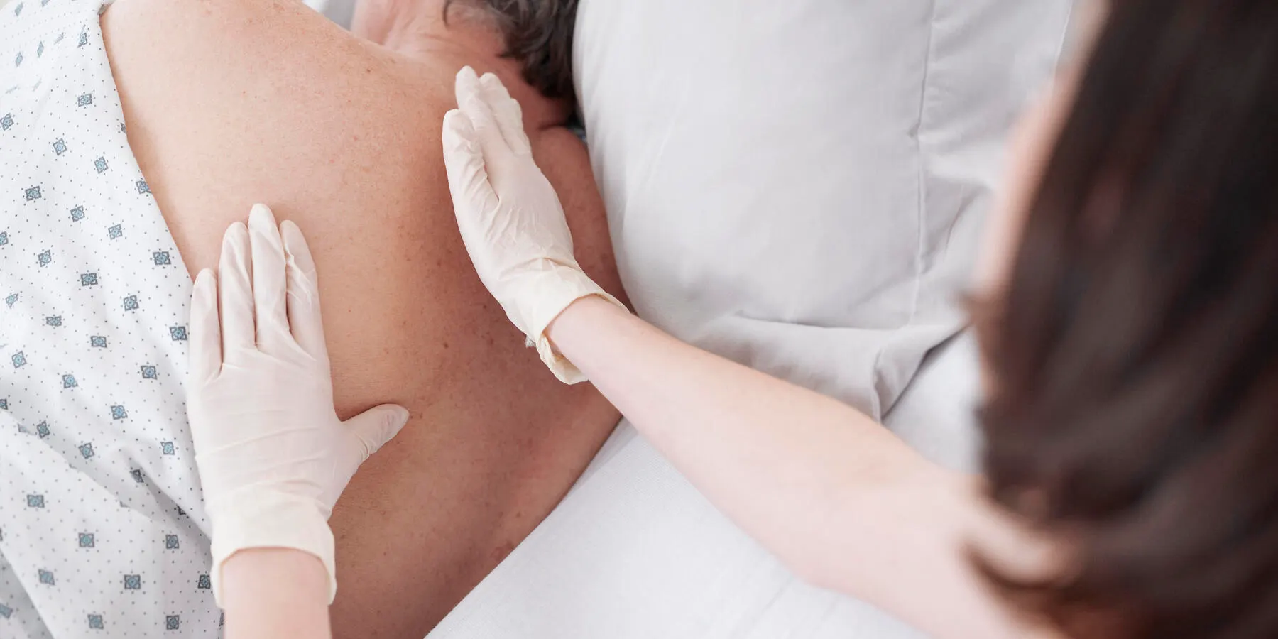 Close-up of nurse wearing gloves touching the back of elderly patient