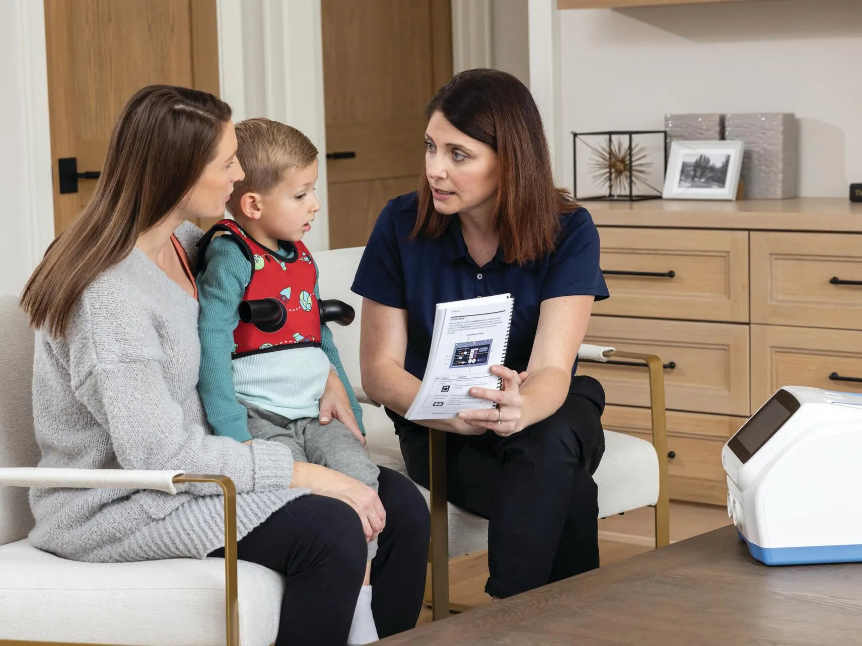 Patient trainer shows a manual to a parent and pediatric patient wearing The Vest in their living room