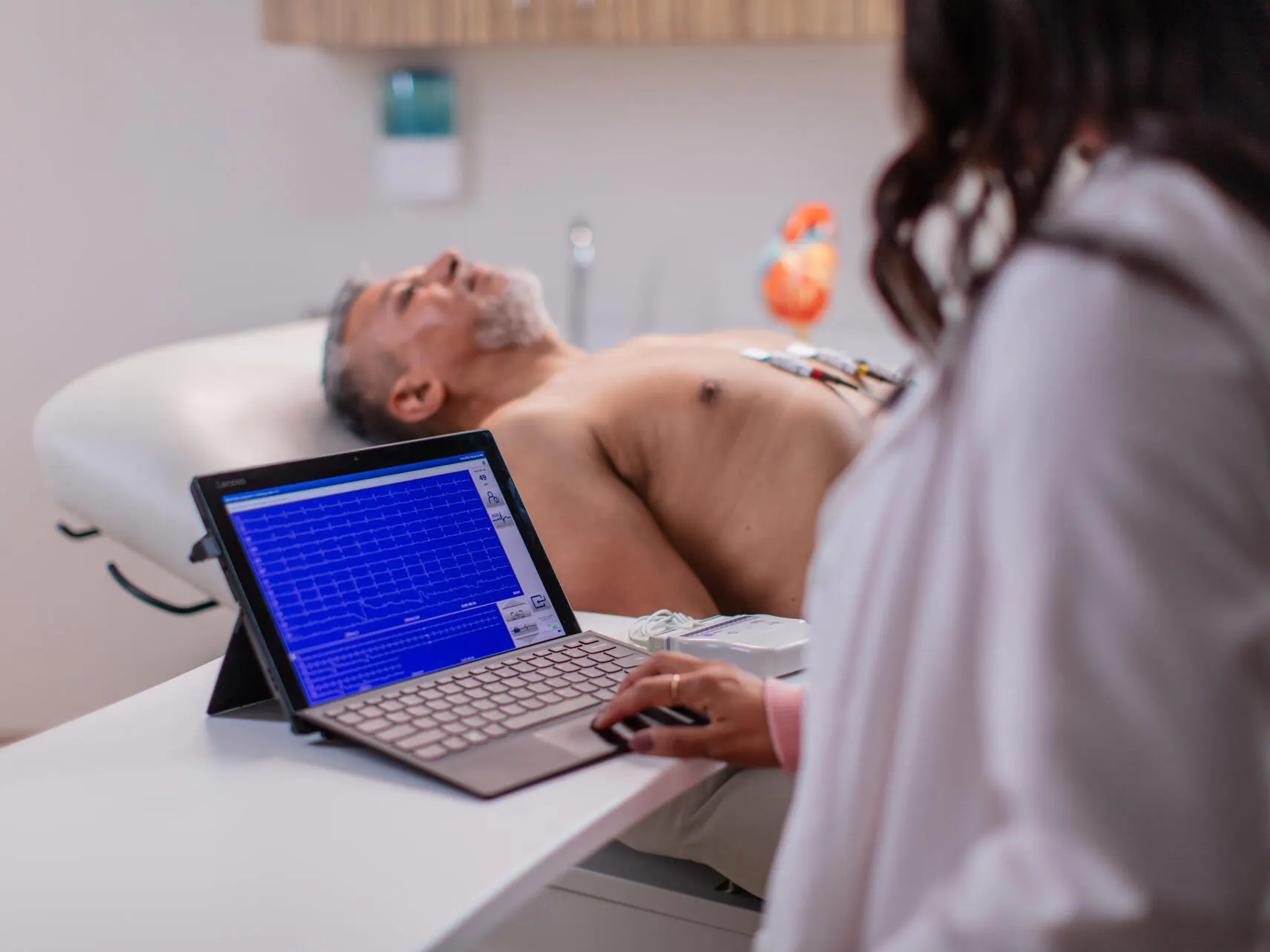 Cardiology Technician examines an ECG next to a patient with electrodes on his chest