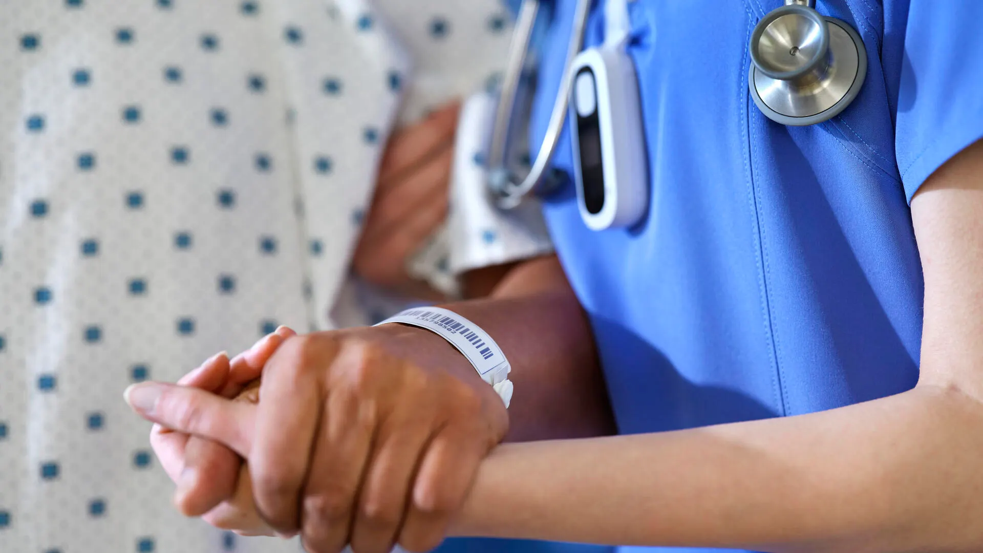 A healthcare worker with a smart badge helps a patient in a hospital gown walk