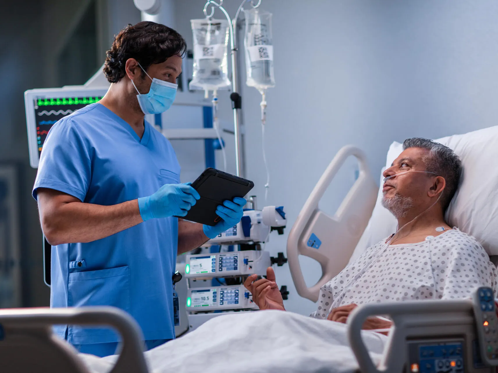 Clinician discusses the contents of a tablet device with a patient who is sitting up in a hospital bed