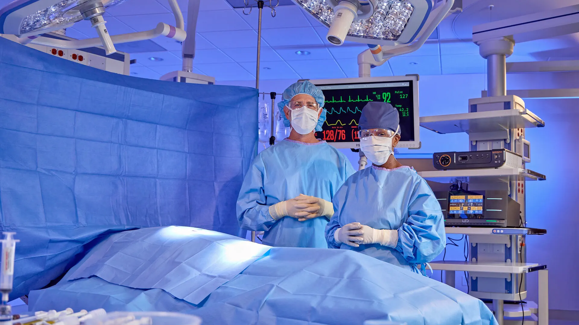 Two surgeons stand in an operating room amongst medical equipment