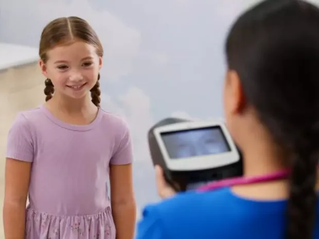 A girl smiling looking at nurse holding the spot vision screener
