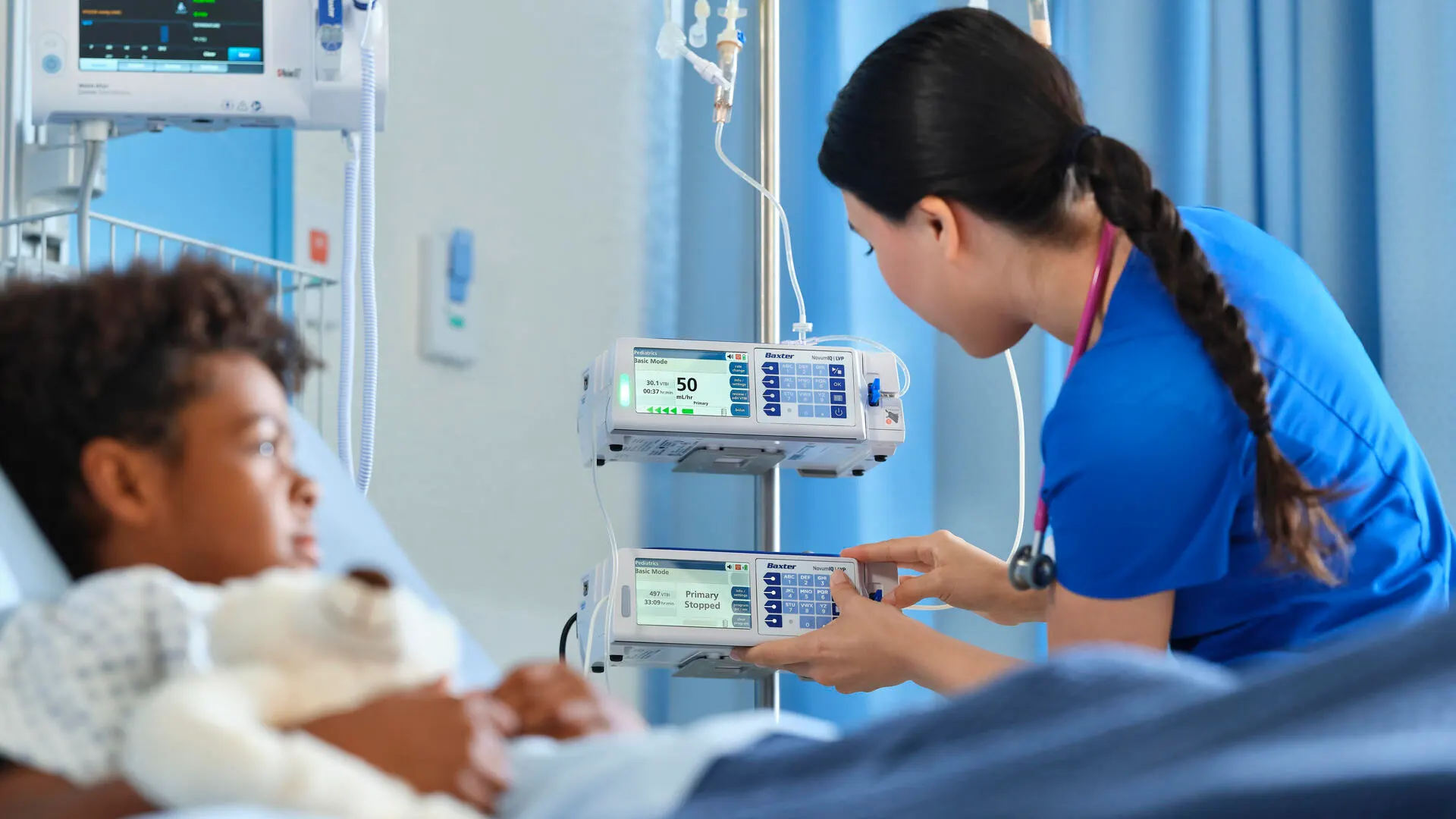 Pediatric patient with tedybear observing how a healthcare profesional adjusts the setitings of a Clinolipid bag syringe pump